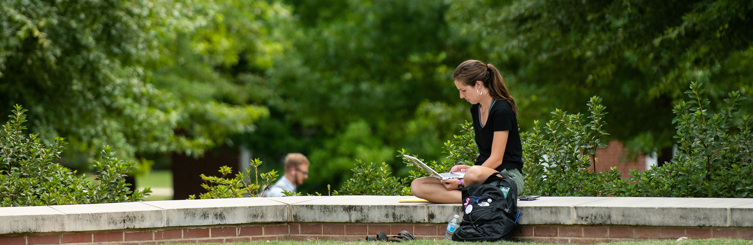 student sitting and studying on a low wall outside