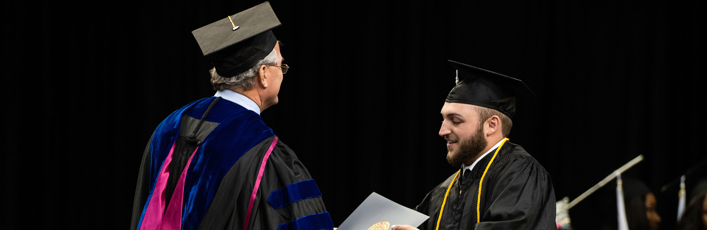 Dean Joe Aistrup hands a student his diploma on stage at graduation