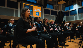 Band members playing clarinets sit in the first row of a symphonic ensemble