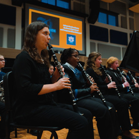 Band members playing clarinets sit in the first row of a symphonic ensemble