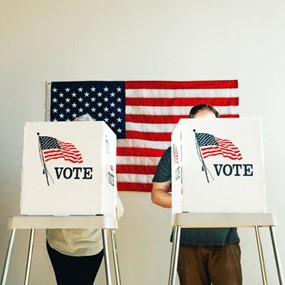 People voting at booths in front of an American flag