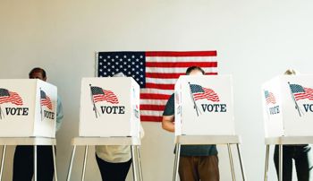People voting at booths in front of an American flag