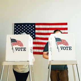 People voting at booths in front of an American flag