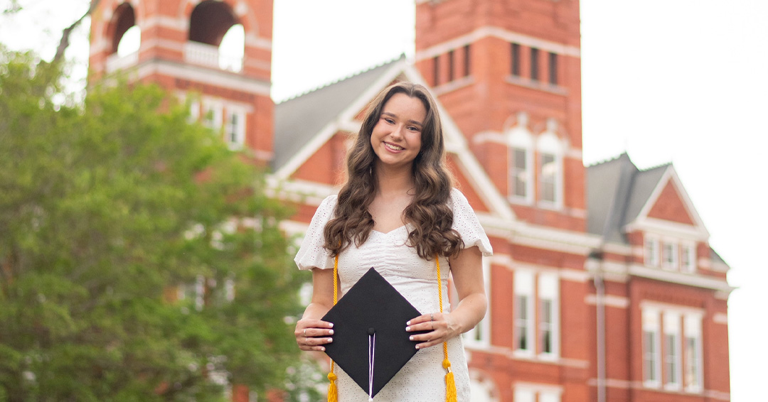 Manna stands in front of Samford Hall holding a graduation cap