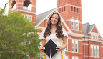 Manna stands in front of Samford Hall holding a graduation cap