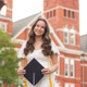 Manna stands in front of Samford Hall holding a graduation cap