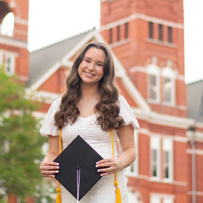 Manna stands in front of Samford Hall holding a graduation cap