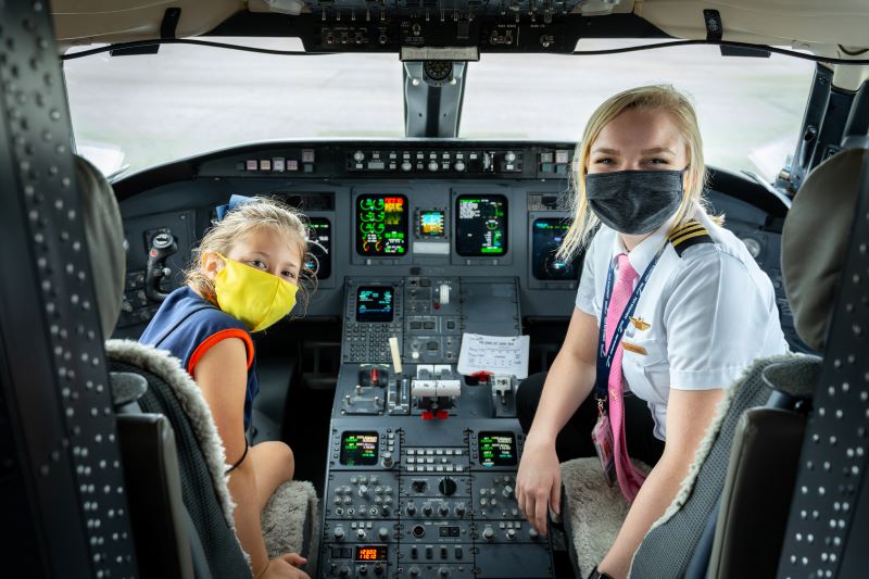 A pilot and young girl in the flight deck of a plane