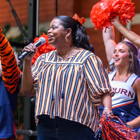 Octavia cheers into a microphone while Aubie and the cheerleaders cheer behind her