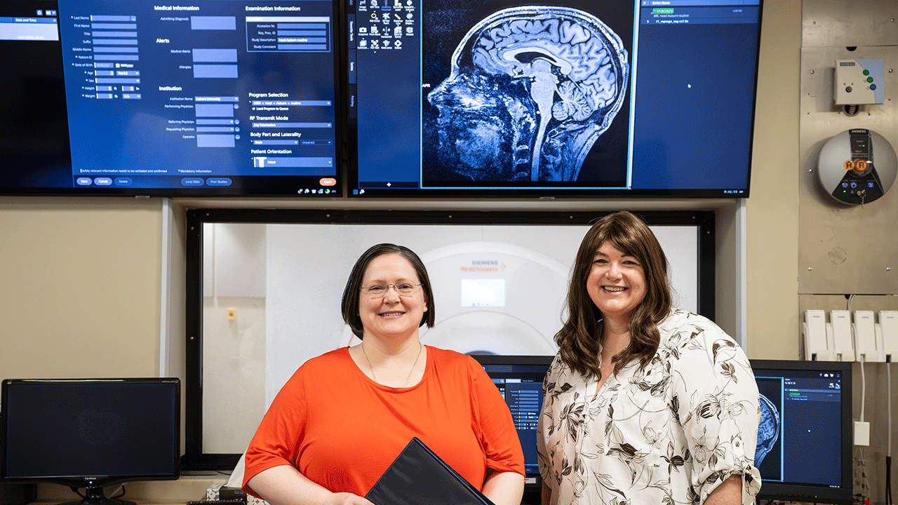 Jennifer Robinson and Meredith Reid stand in front of a screen with an image of the brain.