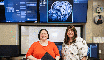 Jennifer Robinson and Meredith Reid stand in front of a screen with an image of the brain.