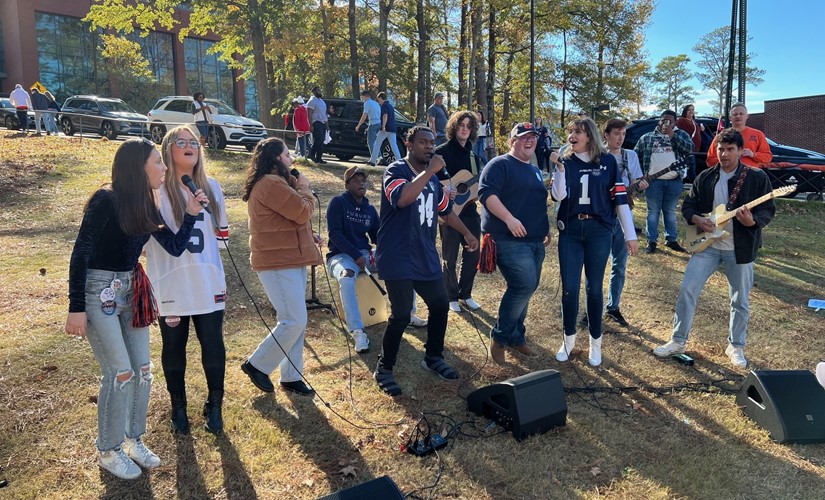 Several people stand around a microphone, speaking to an attentive audience in a vibrant public gathering.