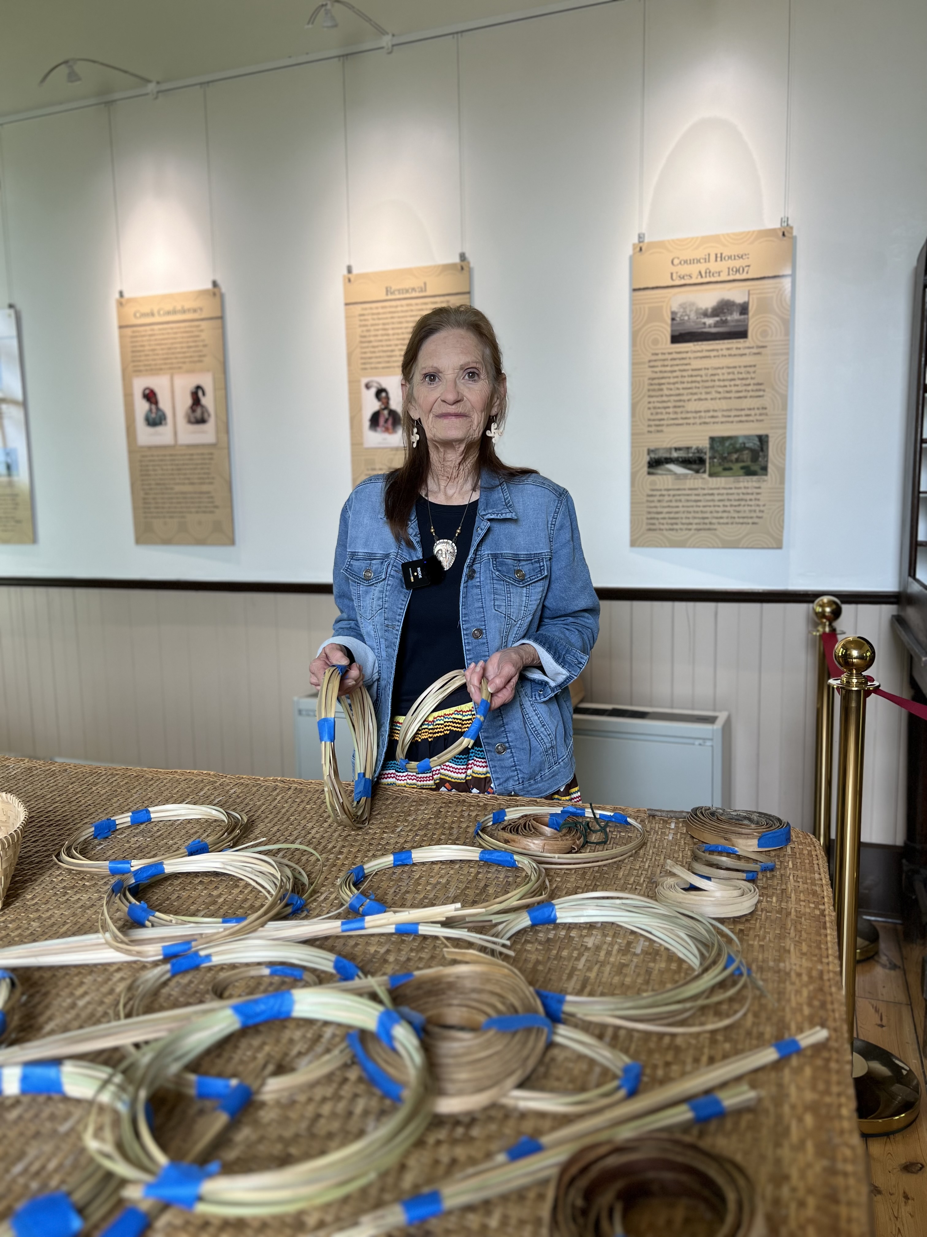 Woman in blue denim jacket holding river cane that has been bundled in circles.
