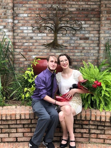 A couple sits on a brick wall in front of foliage