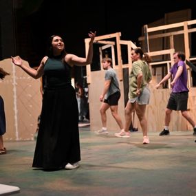 Student actor performing on center stage while dancers move across the background
