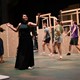 Student actor performing on center stage while dancers move across the background