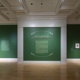 Title wall of Radical Naturalism: Lyric Birdscapes. Walls are an emerald green with light gold text and surrounding leaf graphic elements and white trim