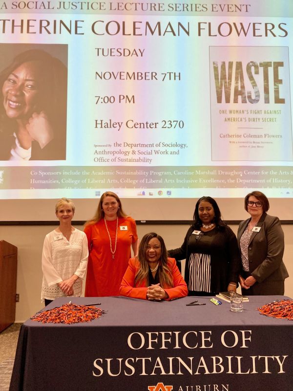 Catherine Flowers sitting at table with Liberal Arts faculty standing around her.