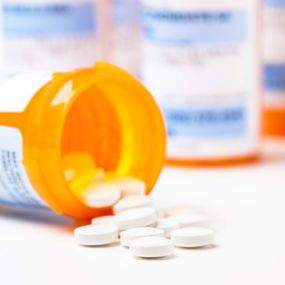 Round white prescription medication pill tablets spilling from a bottle with numerous full bottles in background