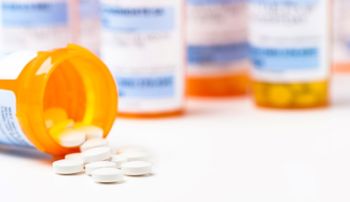 Round white prescription medication pill tablets spilling from a bottle with numerous full bottles in background