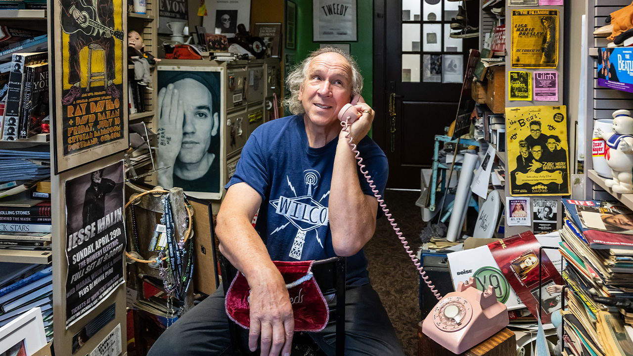 George talks on a pink rotary phone in his crowded office