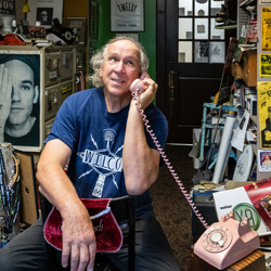 George talks on a pink rotary phone in his crowded office