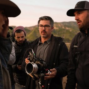 Matt Sakatani Roe holding camera and talking to actors on set