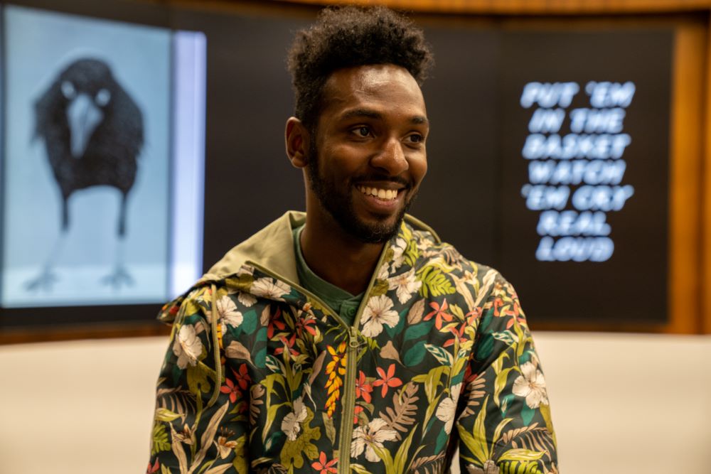 Kofi Bazzell-Smith in front of a digital display of his artwork