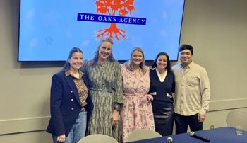 group of people standing in front of a screen with an image of the oaks agency logo