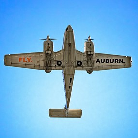 A plane flying overhead with the words "FLY AUBURN" painted on the underside of its wings