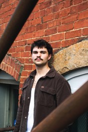 photo of a man in a brown jacket against a brick wall