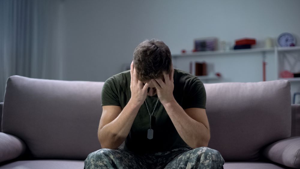 A man in military uniform holds his head in his hands