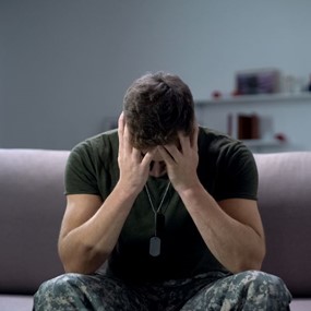 A man in military uniform holds his head in his hands