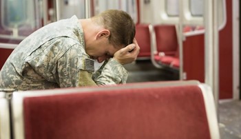 A man in military uniform holds his head in his hands on an empty bus