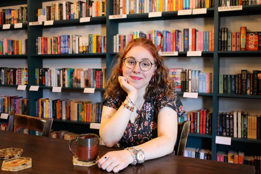 Louise Schulmann-Darsy sits at a cafe with a bookshelf of romance novels behind her