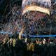 Graduates in caps and gowns reaching for blue and orange confetti at graduation