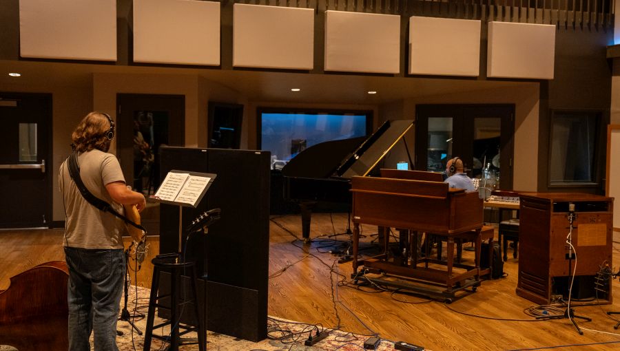 A man playing music in a vibrant recording studio filled with instruments and sound equipment.