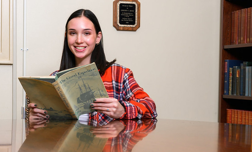 Emma Bond reads The Grand Expedition, a book written by her grandfather, inside the Gordon Crews Bond library