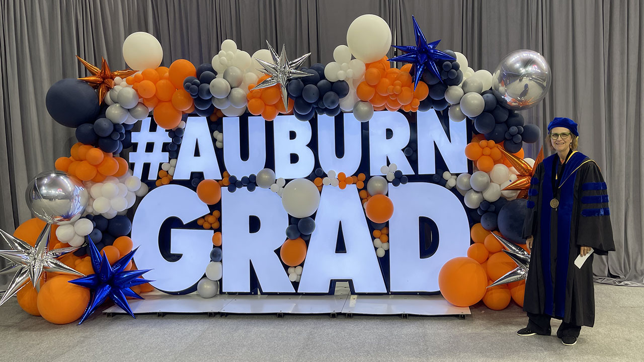 Professor Alice Smith stands beside an Auburn Grad display at graduation