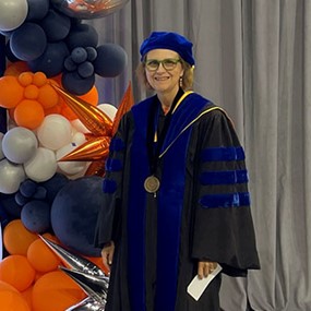 Professor Alice Smith stands beside an Auburn Grad display at graduation