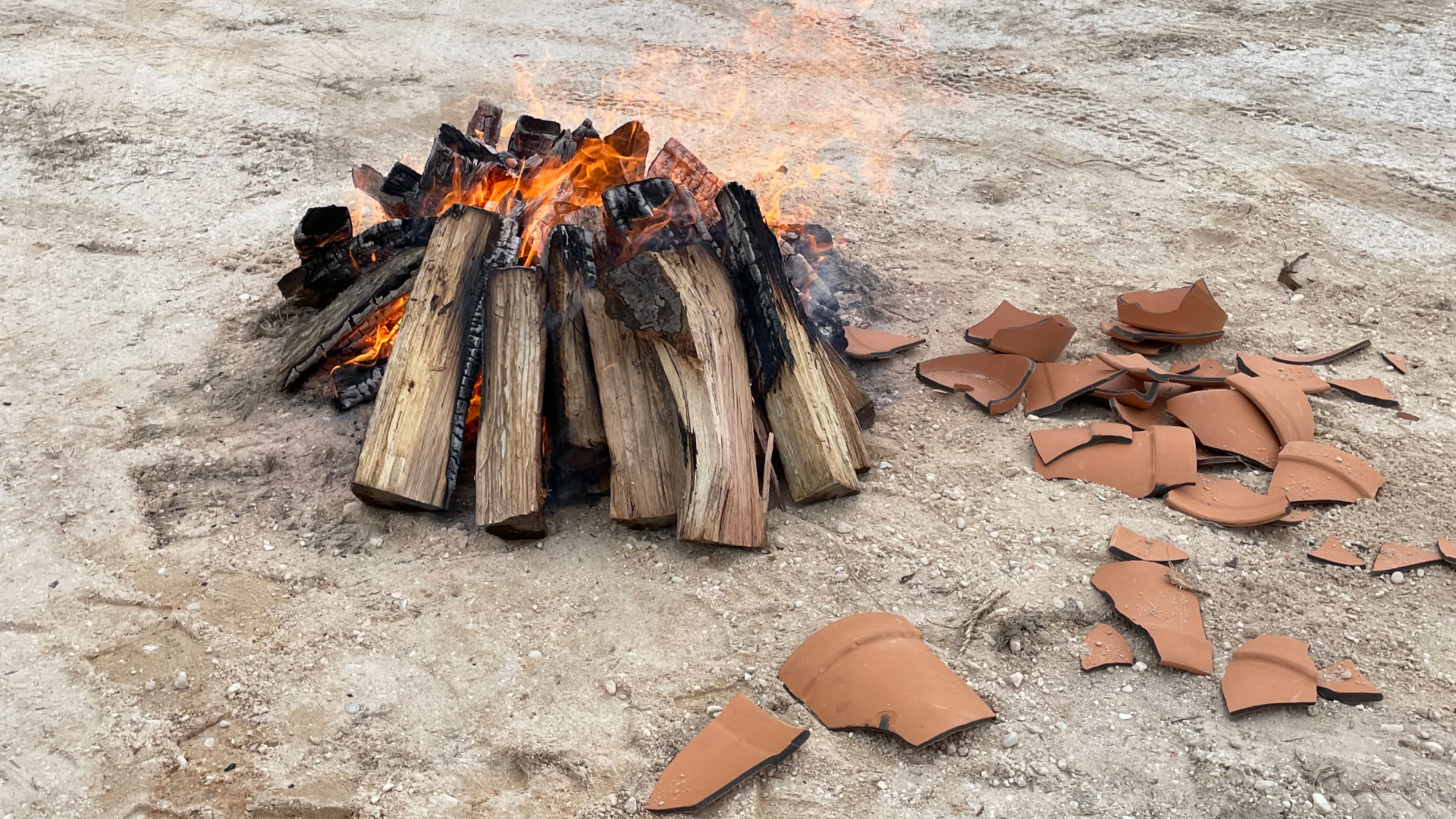 Image of logs on fire with pieces of terra cotta pots on the ground