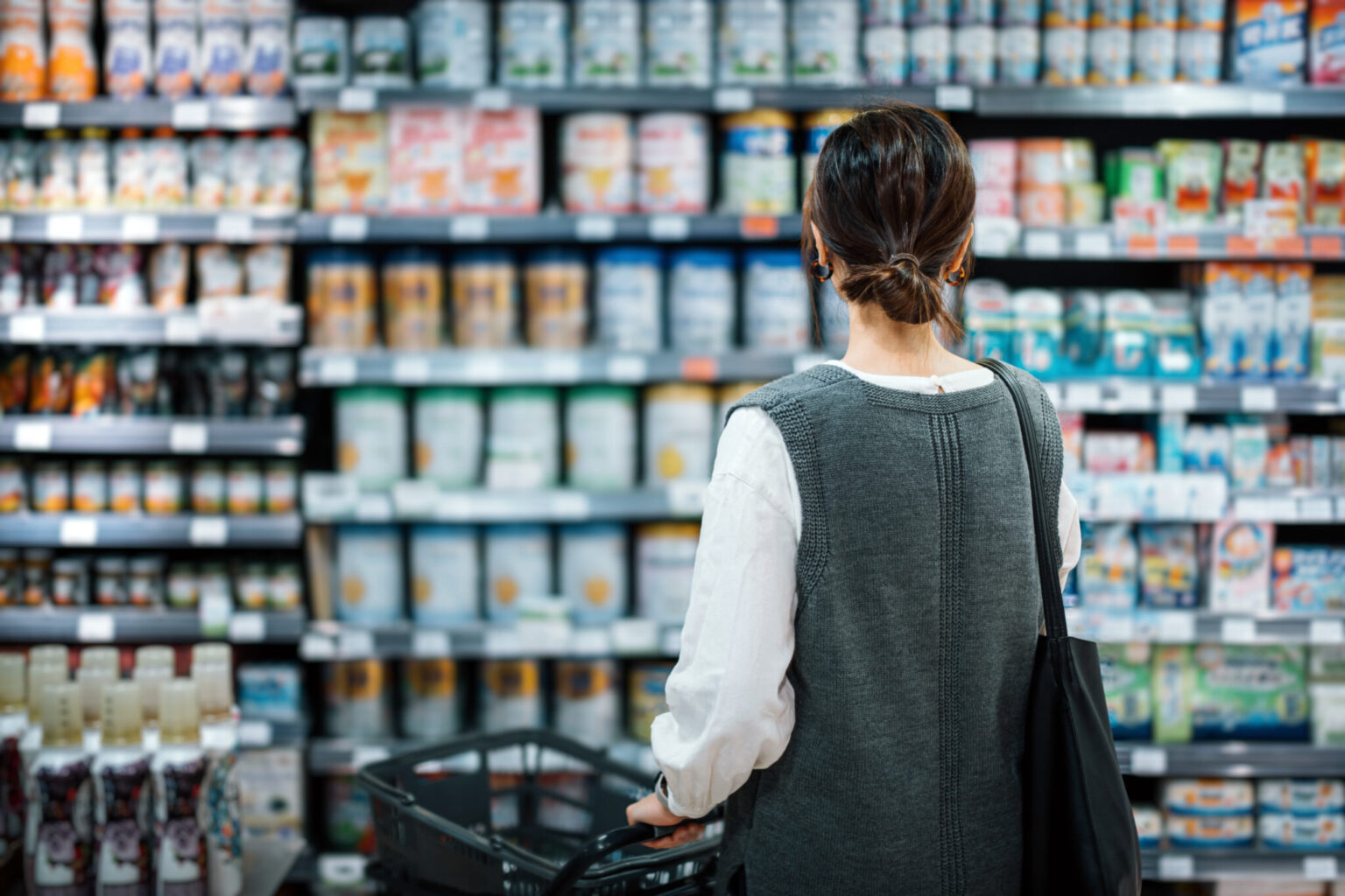 A young mother with a shopping cart grocery shopping for baby products in a supermarket.