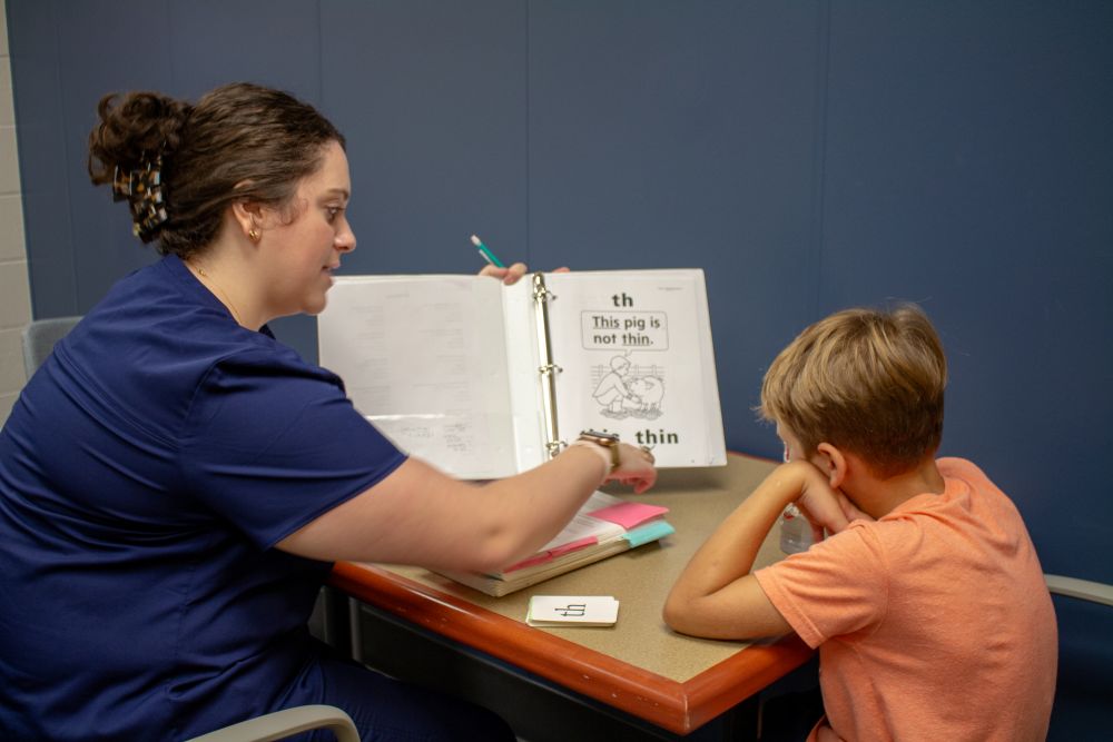 A clinician helping a child read from a practice book