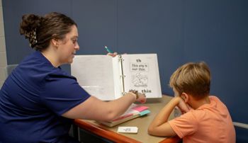 A clinician helping a child read from a practice book