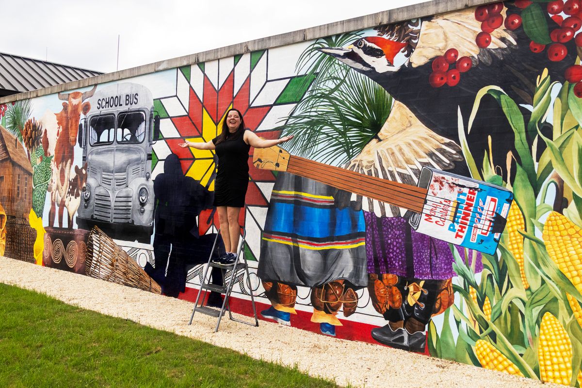 Wendy DesChene installing a 50-foot mural depicting the history and culture of Poarch Creek Indians
