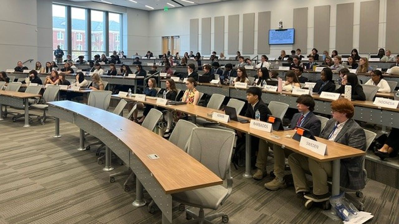 A large group of students seated in a conference room, focused on a presentation or discussion taking place.