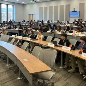 A large group of students seated in a conference room, focused on a presentation or discussion taking place.