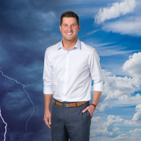 Stephen Neslage posing for photo. On his left, a thunderstorm darkens the sky. On his right, clouds drift across a blue sky.
