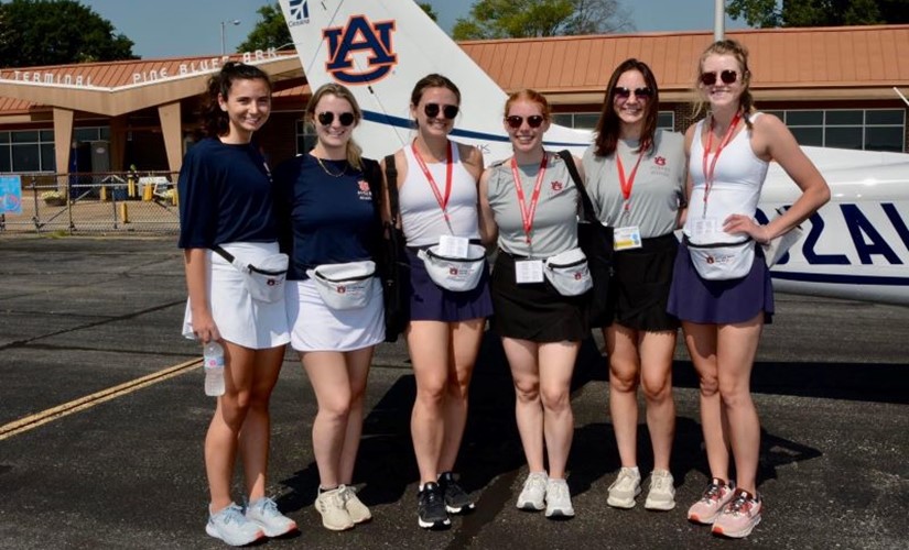 The War Eagle Women stand in front of an Auburn airplane at the airport