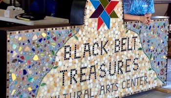 Linda Muñoz, a glass mosaic artist in North Alabama, stands with Black Belt Treasures' sign